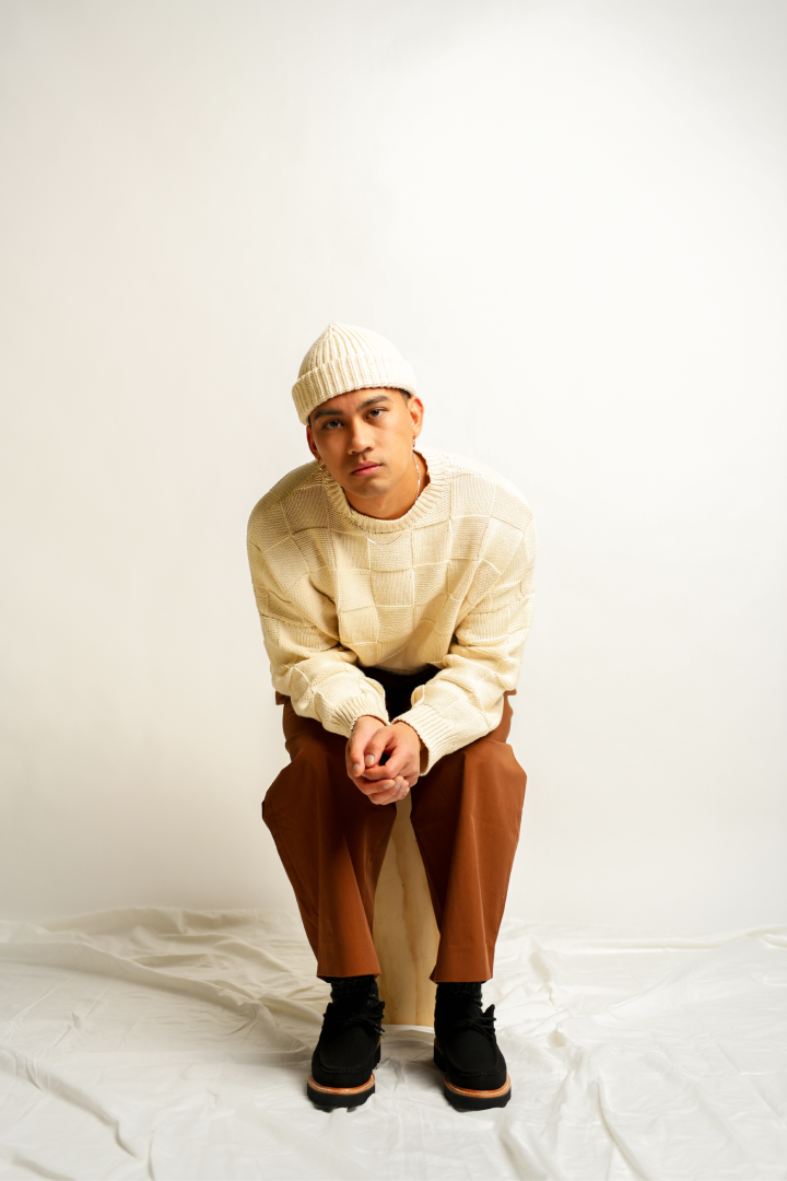 Man sitting wearing beanie, knitted sweater, and truffle pants